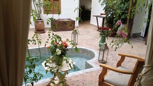 A courtyard with a fountain, potted plants, and a wooden chair. - Riad le Coq Fou (Marrakech)