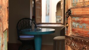An open wooden door leading to a room with a checkered floor, a blue table, and a chair. - Riad le Coq Fou (Marrakech)