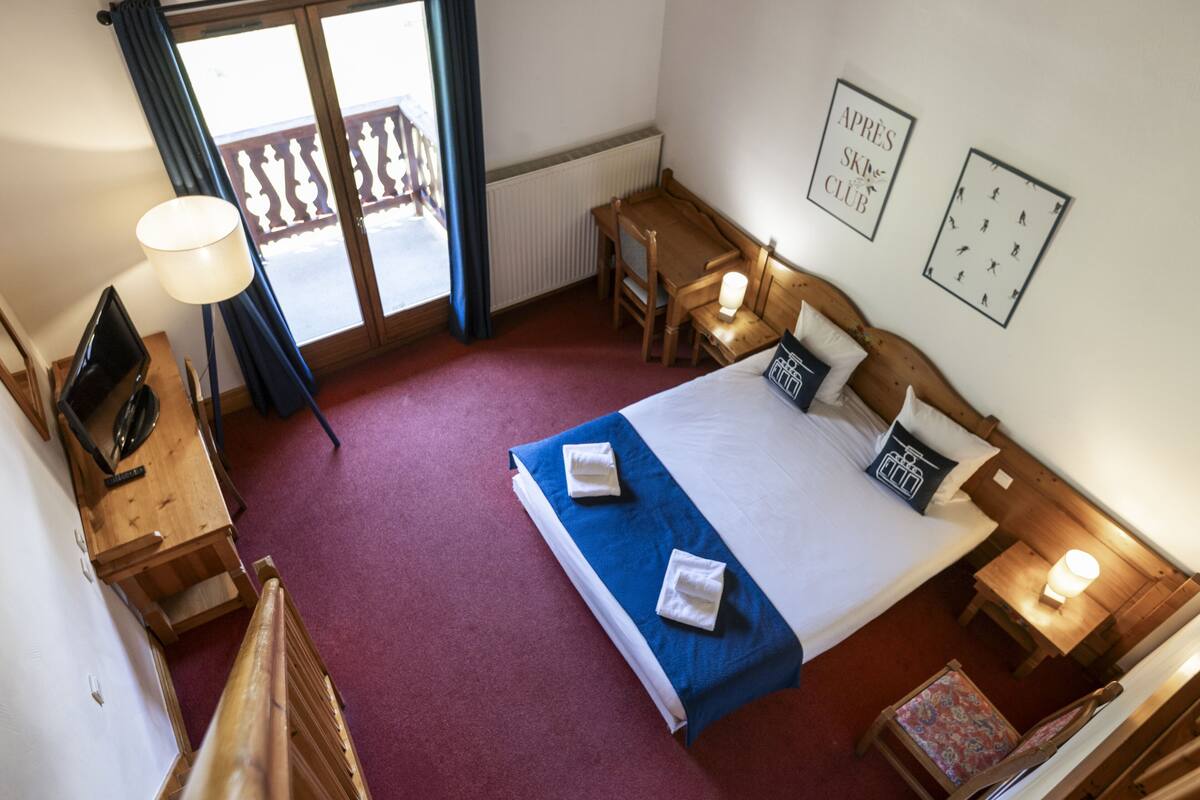 A hotel room with a bed, a desk, a chair, a TV, and a balcony.