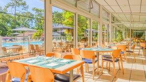 Un restaurante con terraza exterior con vistas a una piscina, grandes ventanales y una vista de árboles.