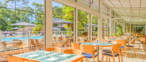A restaurant with outdoor seating overlooking a pool, large windows, and a view of trees.