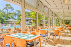 A restaurant with outdoor seating overlooking a pool, large windows, and a view of trees.