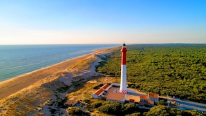 Un faro con estructura roja y blanca, ubicado en una playa con un área boscosa cerca.
