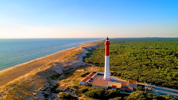 A lighthouse with a red and white structure, situated on a beach with a forested area nearby.