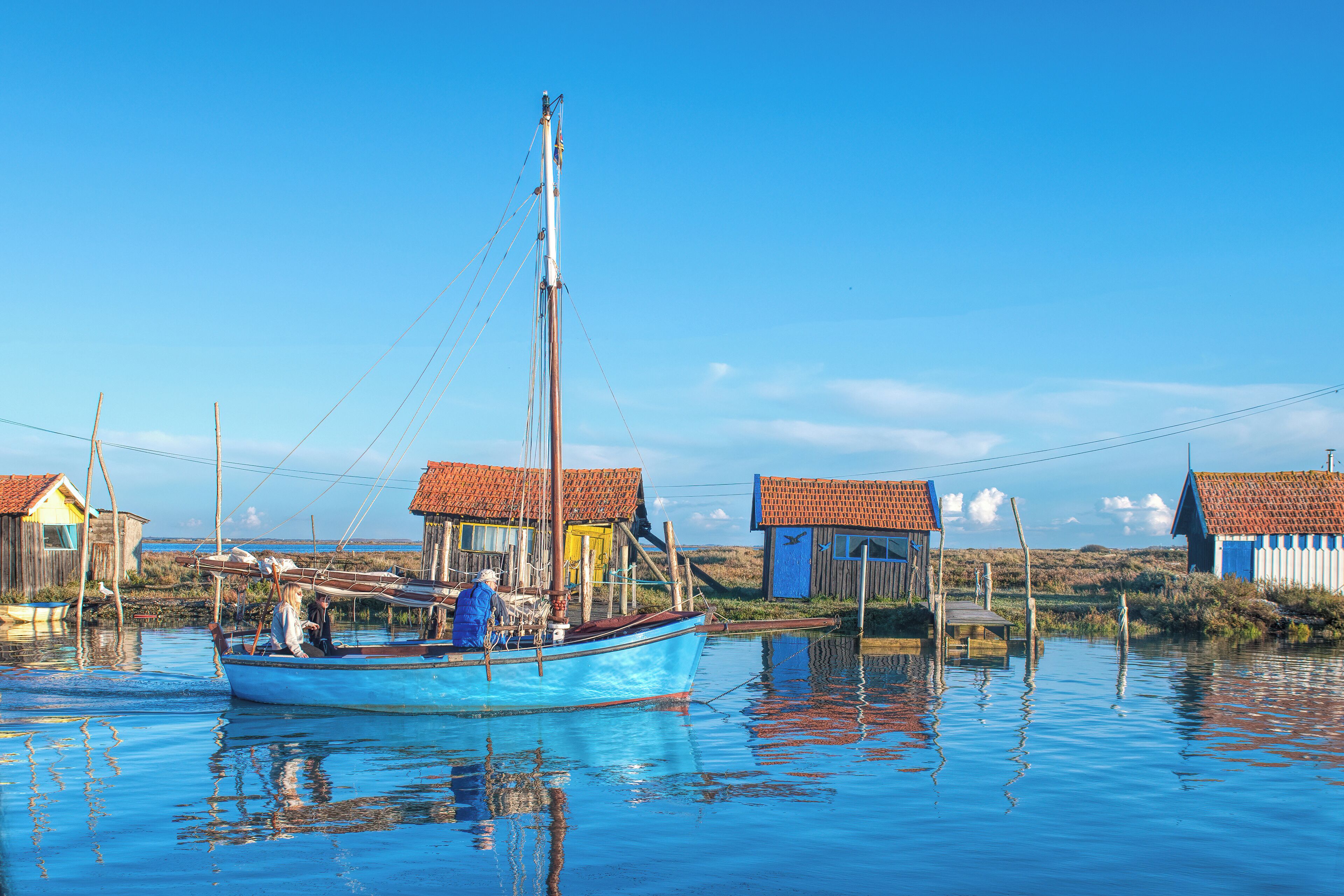 A traditional wooden boat docked at a calm waterway with small houses with red roofs in the background.