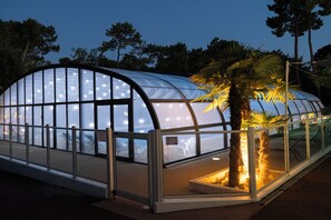 A greenhouse structure with a curved glass roof, surrounded by a metal railing, and a palm tree in the foreground. - Azureva Ronce Les Bains (La Tremblade)