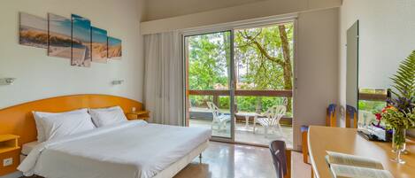 Una habitación de hotel con cama, escritorio y vistas a un balcón con mobiliario exterior.