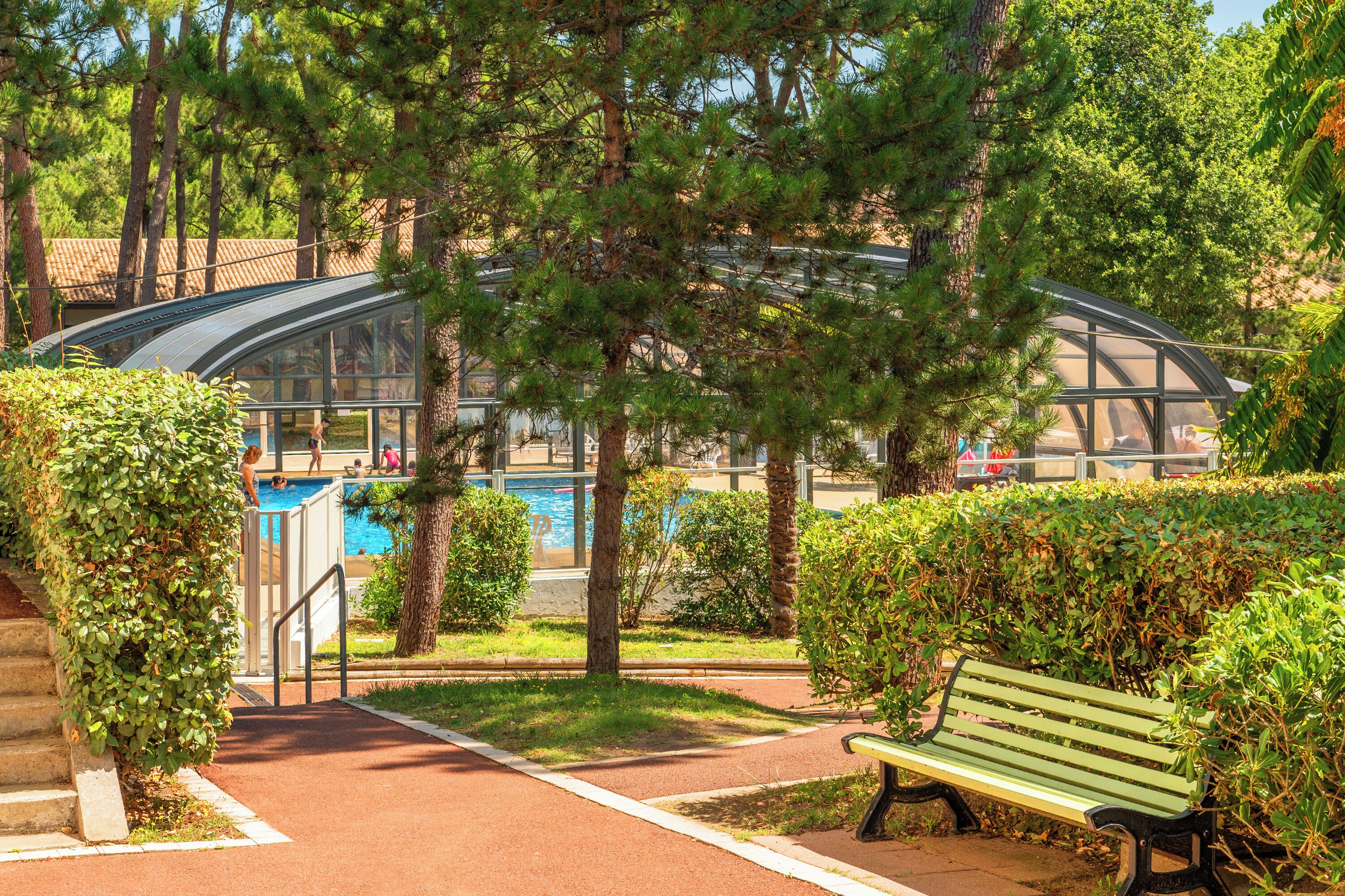 Un parque con piscina, una estructura de vidrio y un banco verde.