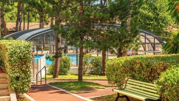 Un parc avec une piscine, une structure en verre et un banc vert.