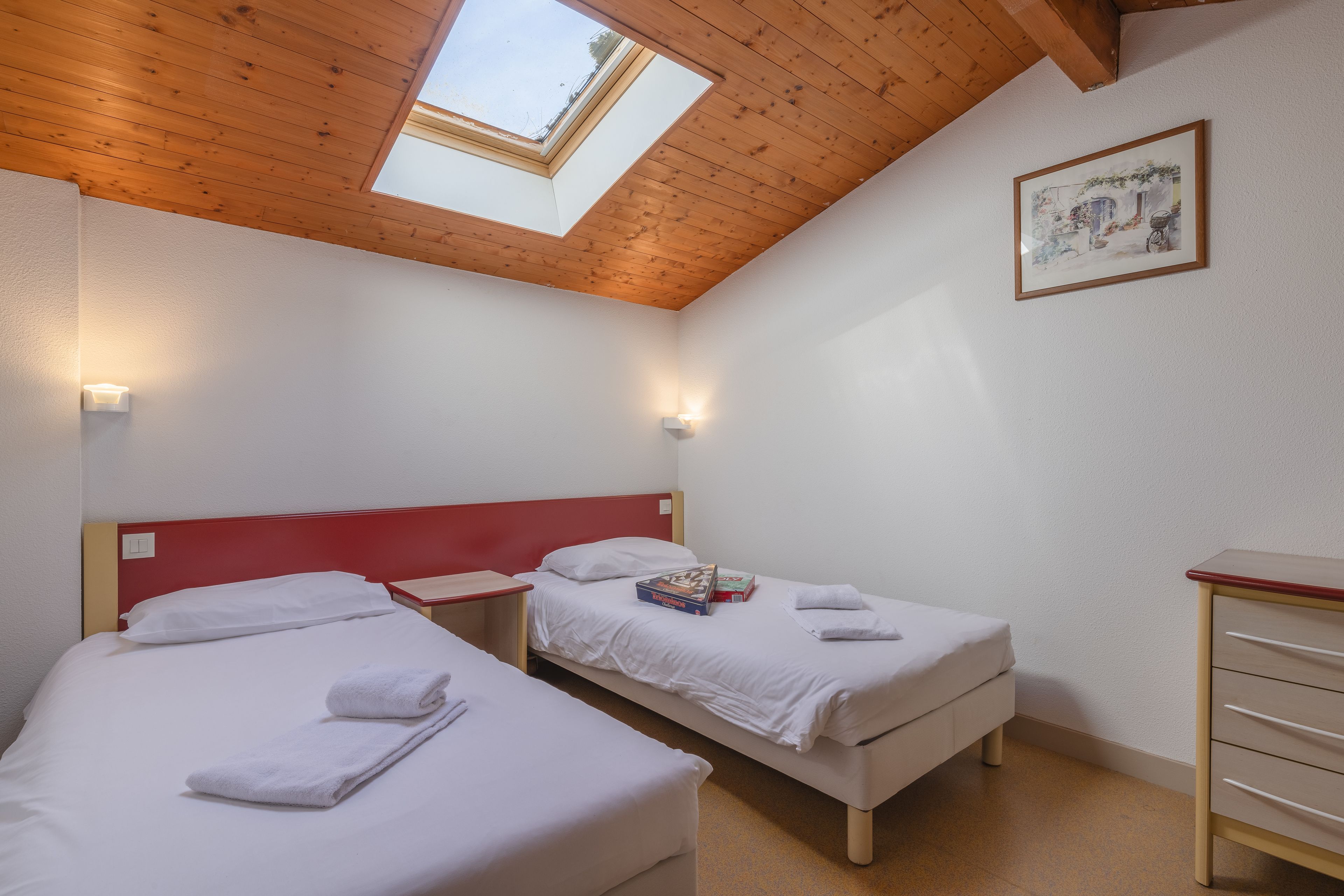 Een kamer met twee bedden, houten balken in het plafond, een dakraam en een ingelijste foto aan de muur.