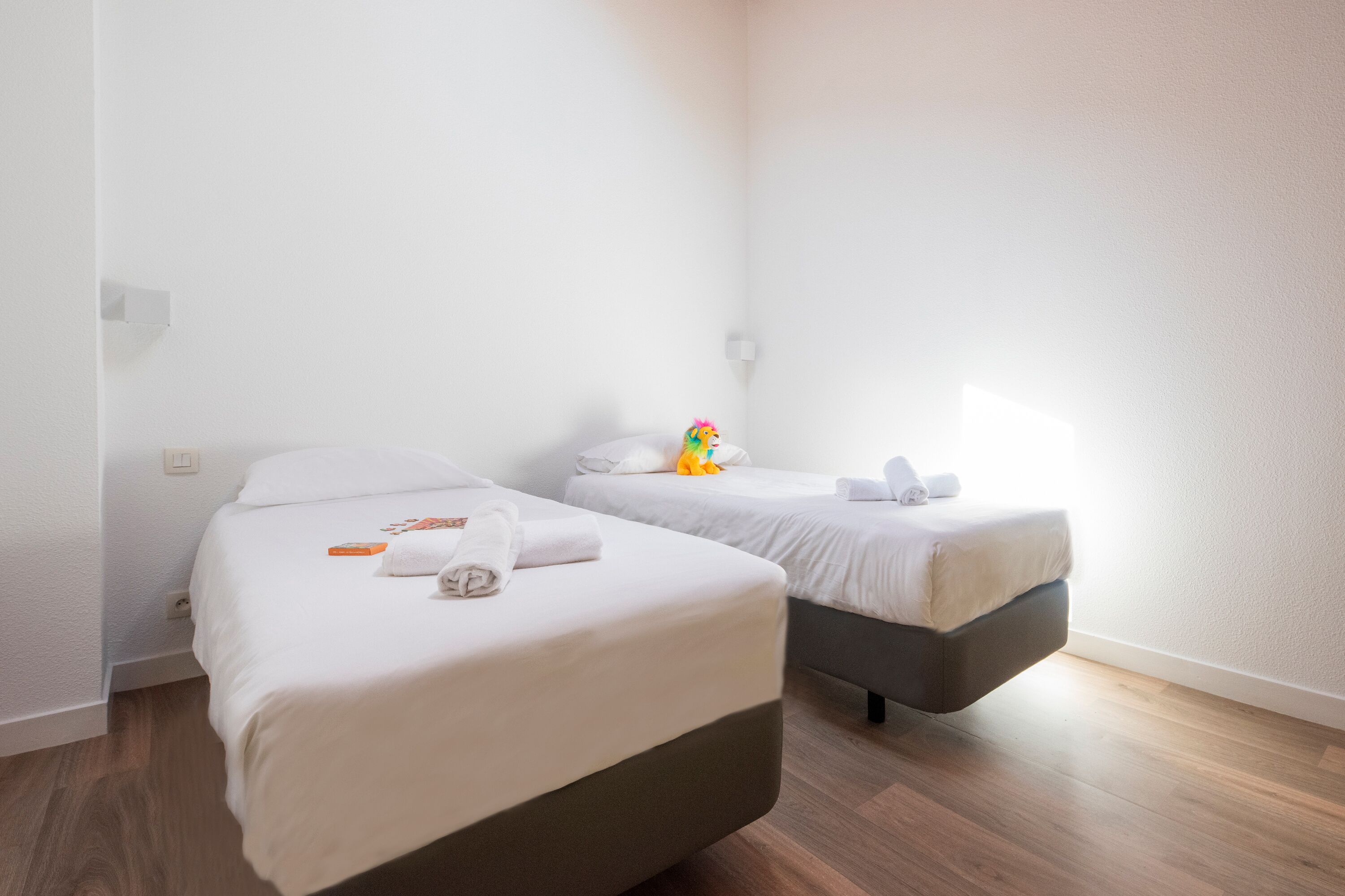 A hotel room with two beds, each with white linens and a small toy on one bed.