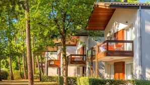 Una hilera de edificios modernos de dos pisos con balcones, rodeados de árboles y vegetación.