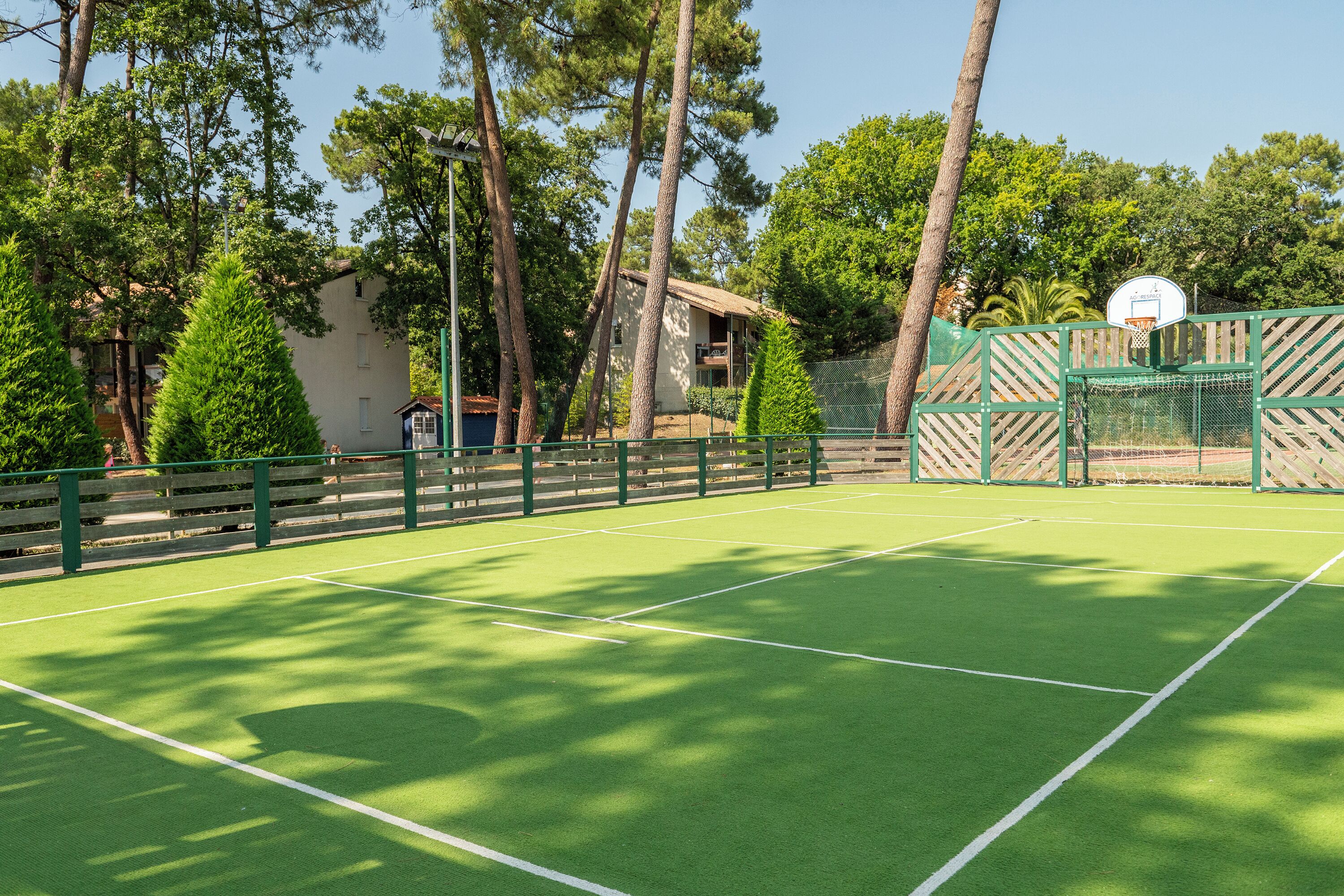 Un court de tennis en plein air, doté d’une surface verte, entouré d’arbres et d’une clôture en bois.