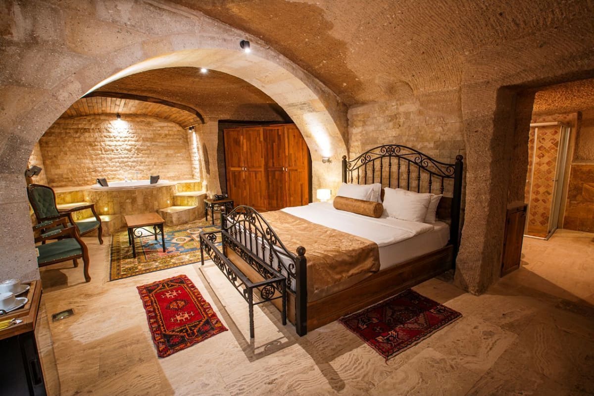 Een slaapkamer met een stenen muur, een houten bed, een stoel, een tafel en een kleine badkamerruimte.