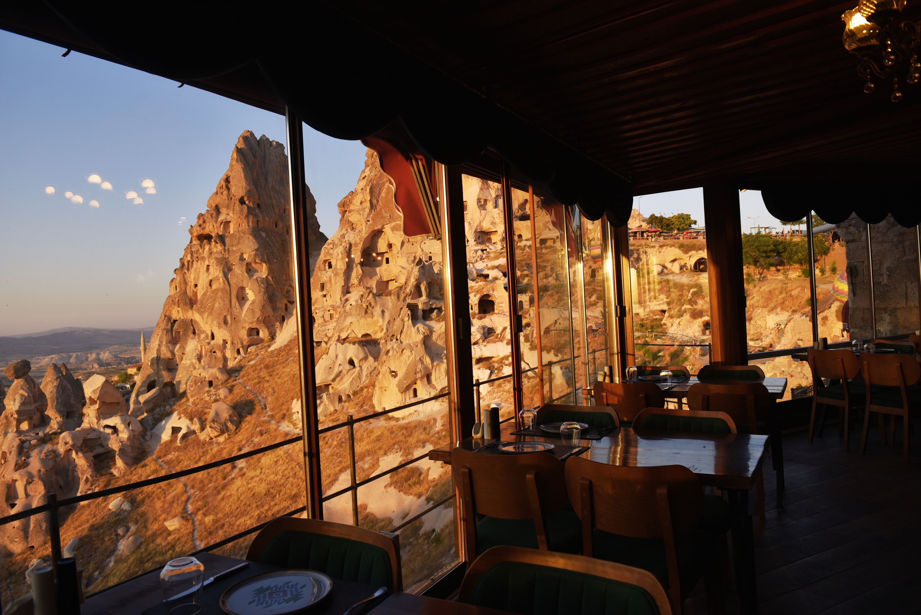 Un restaurant doté de grandes fenêtres offrant une vue sur des formations rocheuses. Des tables et des chaises sont disposées à l’intérieur.