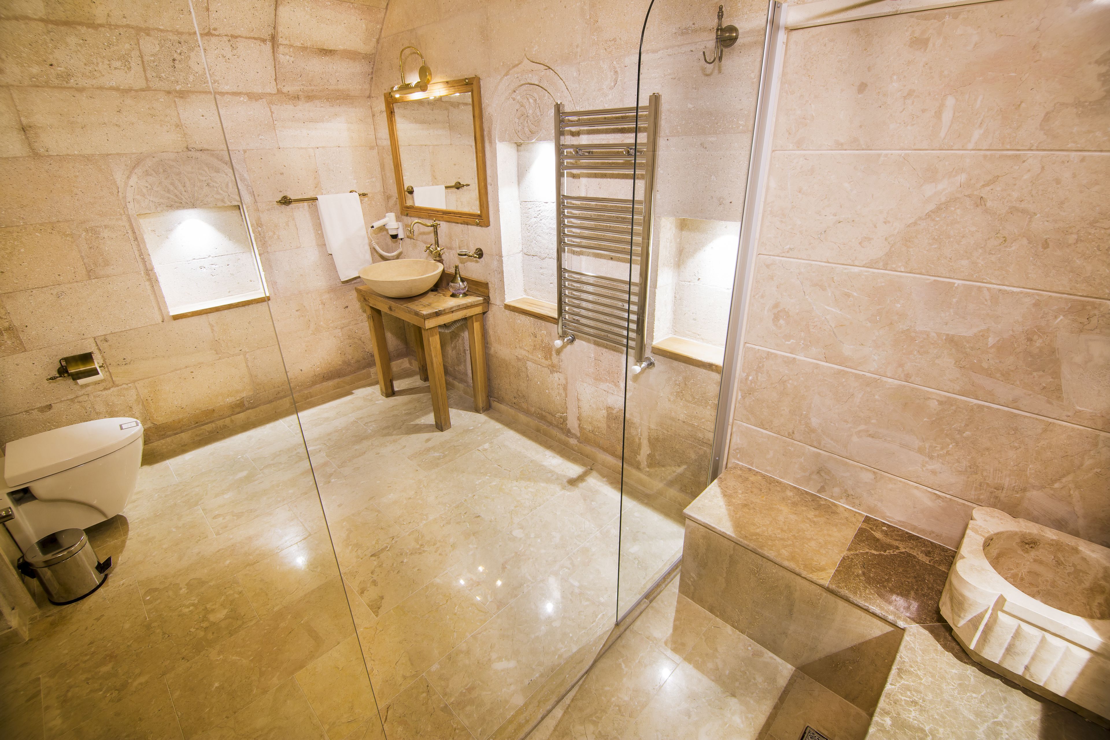 A bathroom with a marble floor, a sink, a toilet, a glass-enclosed shower, and a towel rack.