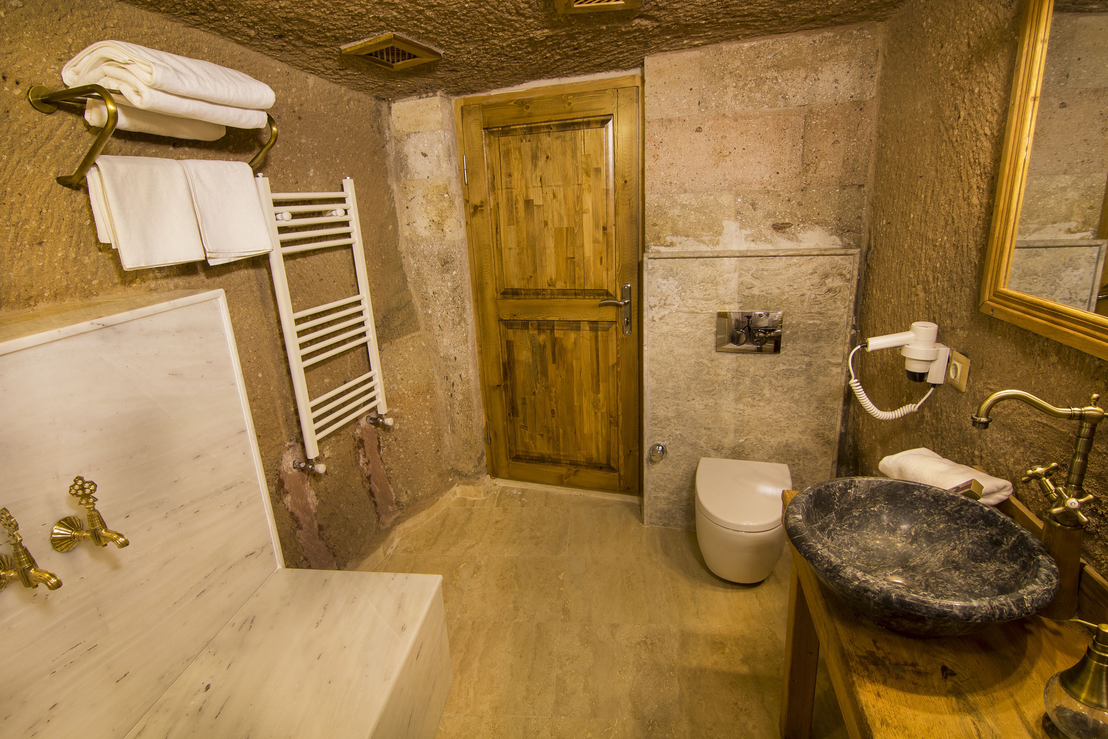 A bathroom with a wooden door, a white toilet, a black sink, and a white bathtub.