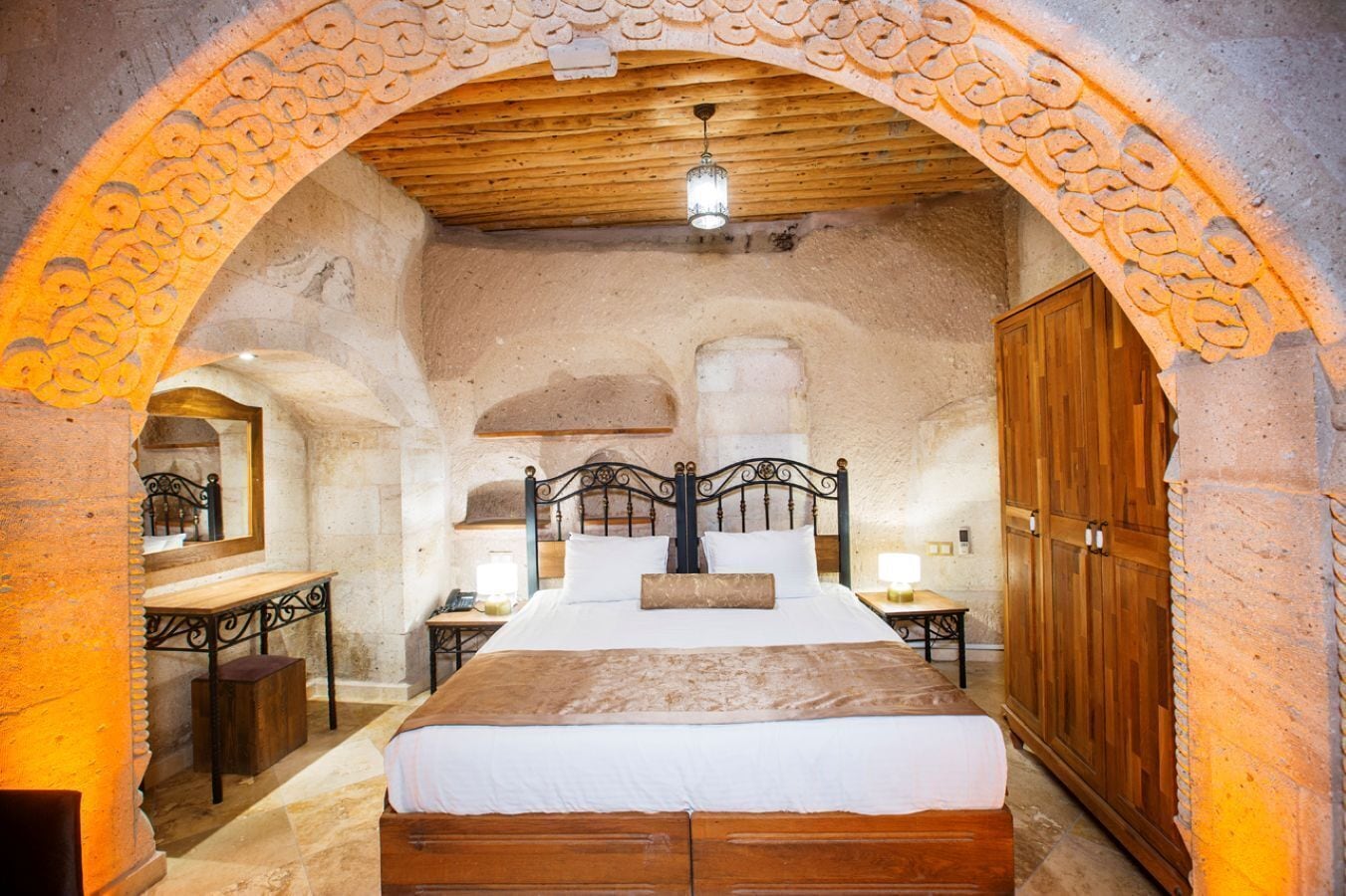 A rustic bedroom with a wooden bed, a nightstand, a mirror, and a wardrobe.