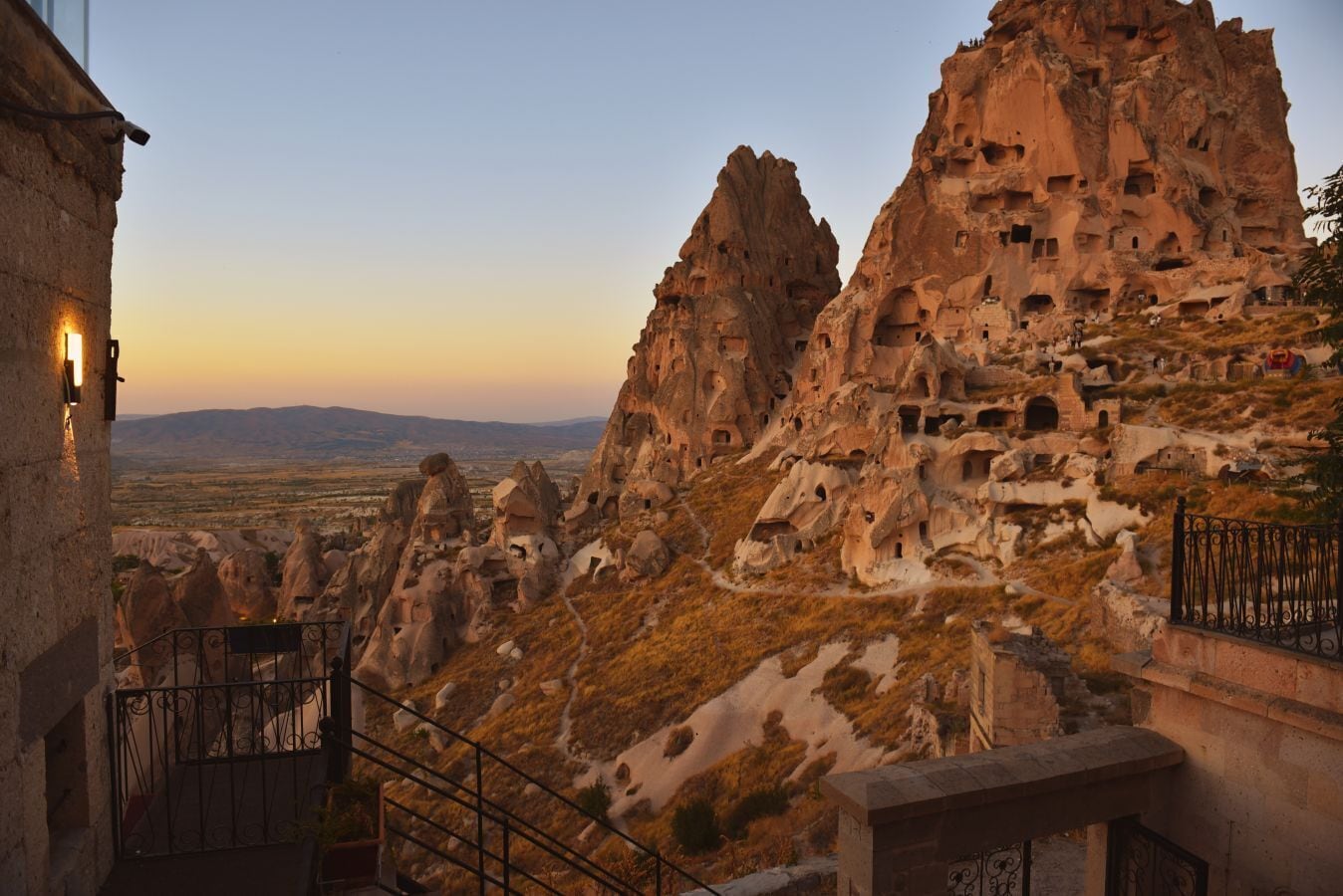 A view of rock formations with numerous cave dwellings, a paved pathway, and a railing.