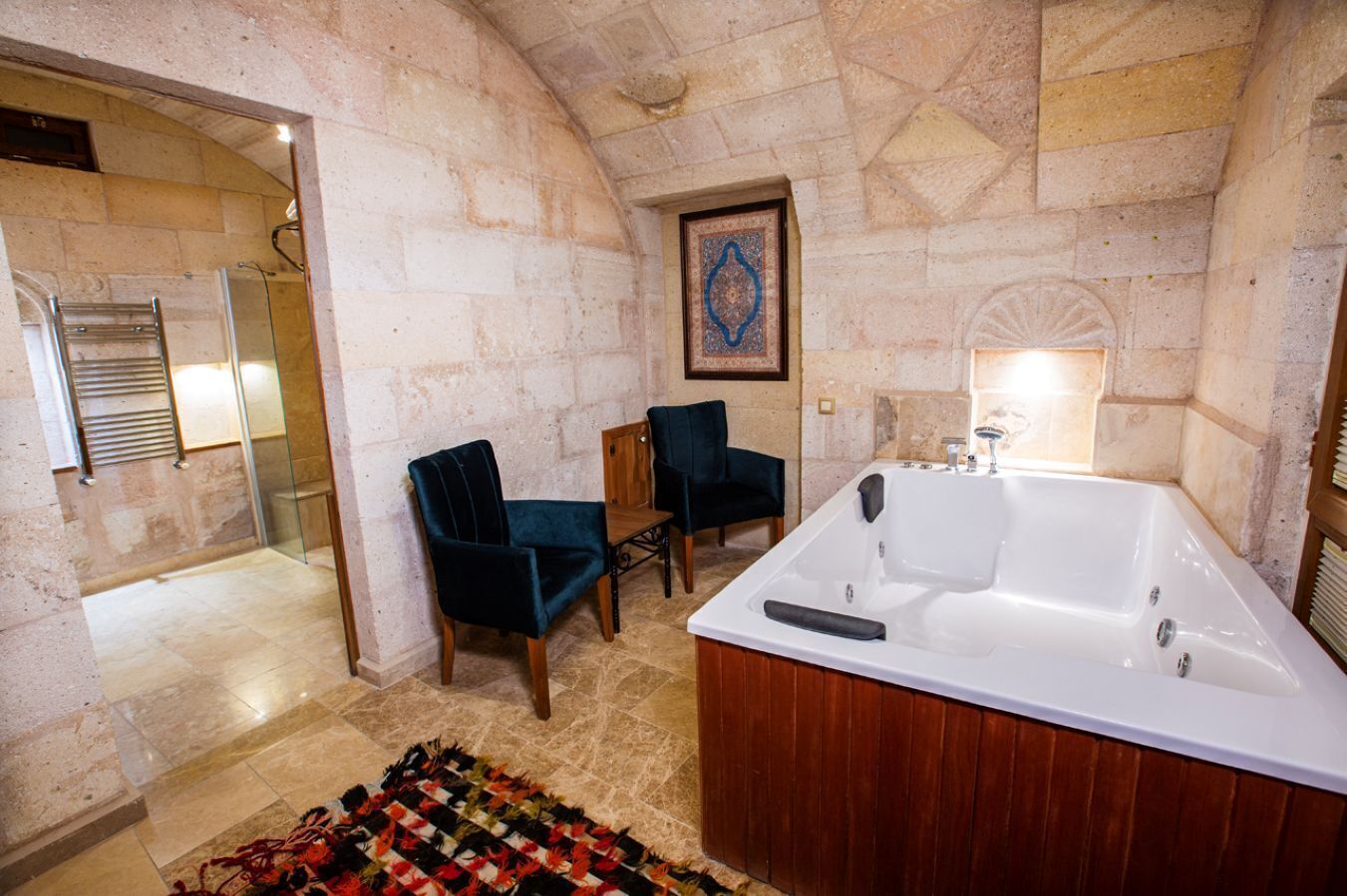 Une salle de bain avec une grande baignoire, deux chaises, une table en bois et un tapis à motifs.