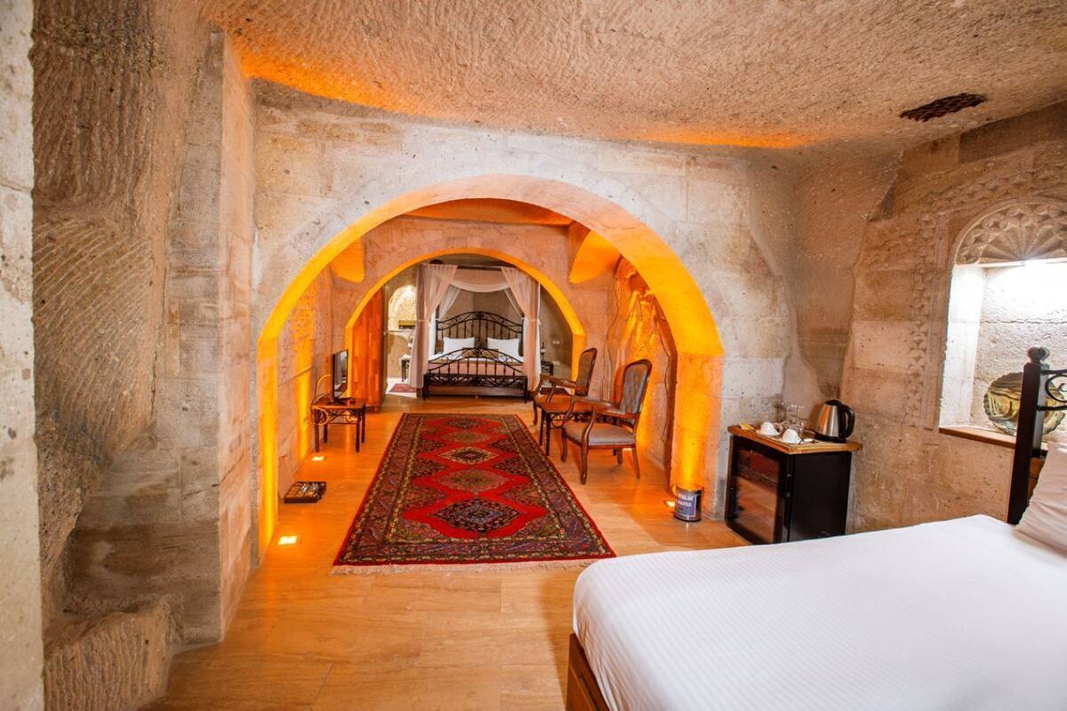 Een slaapkamer met een groot bed, een houten vloer en een rood tapijt met een patroon. Er is een raam met uitzicht op het omliggende landschap.