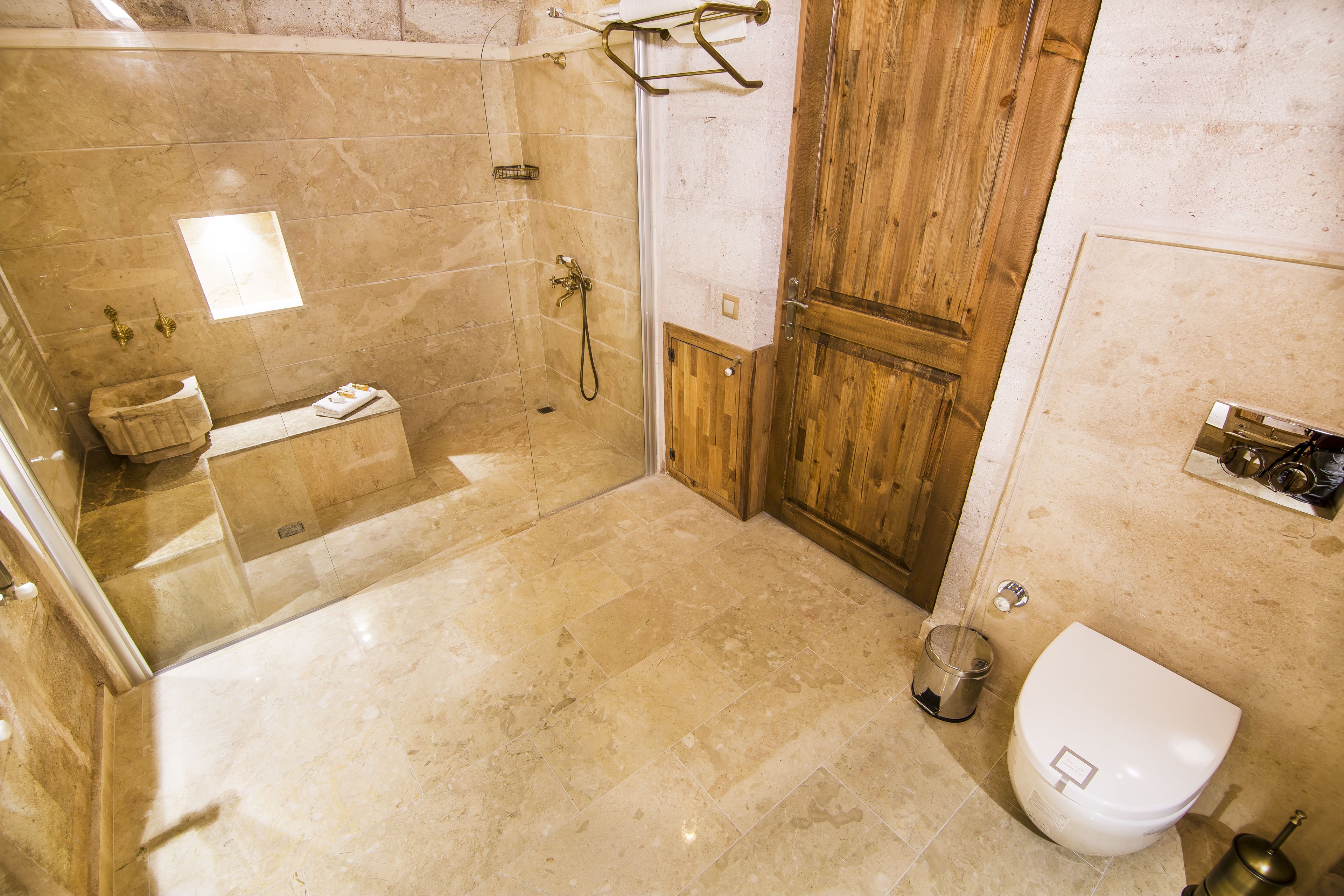 A bathroom with a glass-enclosed shower, a wooden door, a toilet, and a sink with a towel.