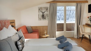 A hotel room with a bed, a sofa, a small table with a glass of wine, and a window with a view of snow-covered trees.