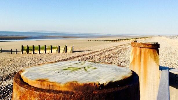 A wooden post with a circular cutout, a sandy beach, and a wooden fence in the background. - Humphries Cross Apartments (Rye)