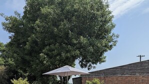 An outdoor patio area with a table and chairs under a large umbrella, surrounded by potted plants and a brick wall. - Humphries Cross Apartments (Rye)