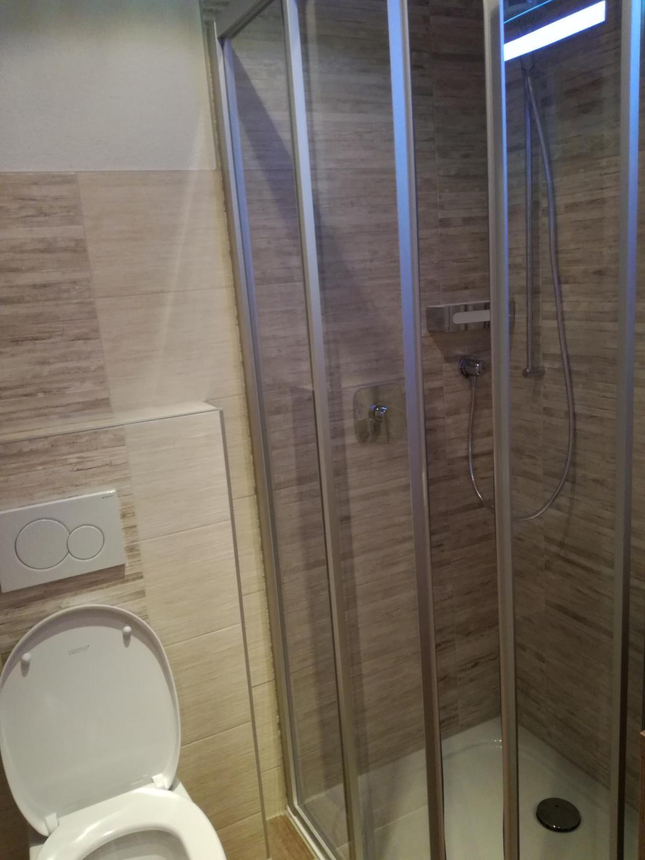 A bathroom with a toilet, a glass-enclosed shower, and a wall-mounted heater.