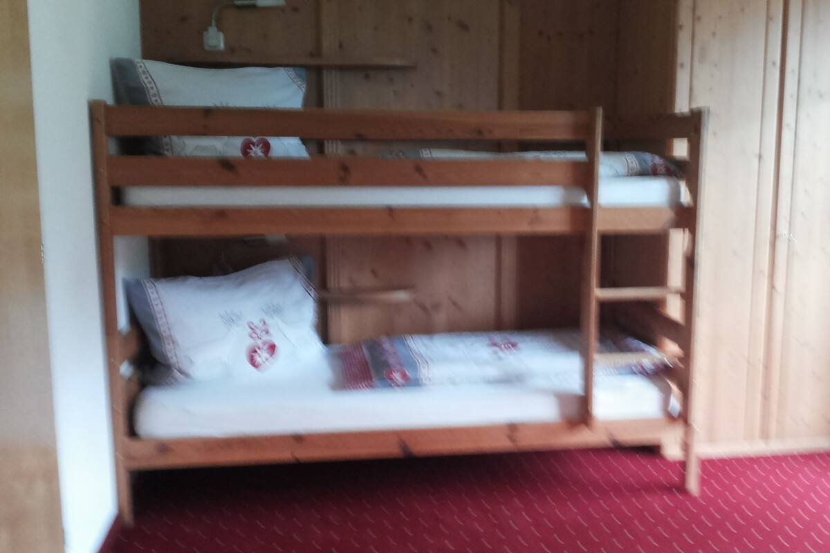 A bunk bed with two levels, a wooden headboard, and a red patterned carpet.