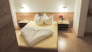 Une chambre d’hôtel avec un lit, deux tables de chevet, une tête de lit en bois et un petit vase avec des fleurs.