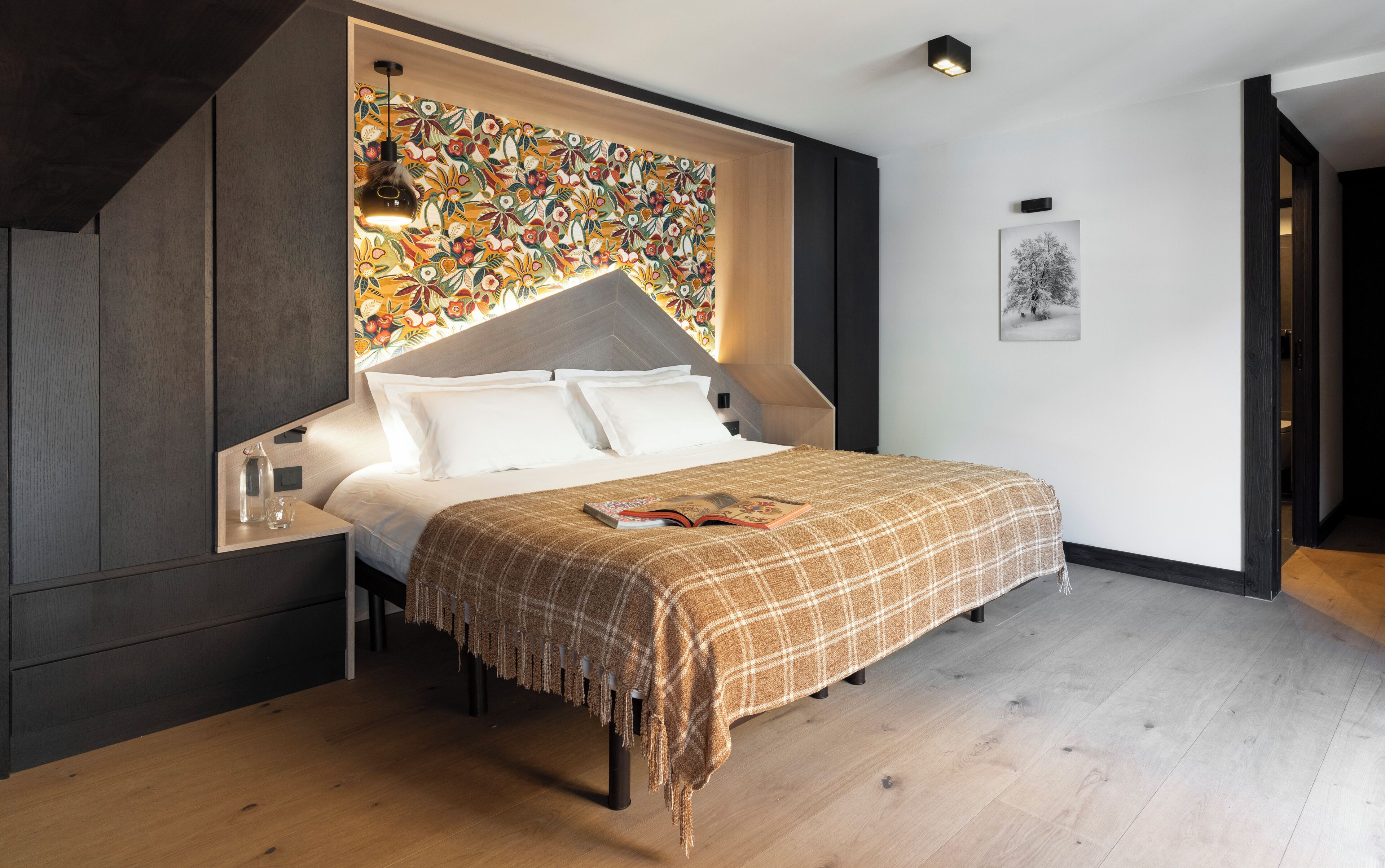 A modern bedroom with a bed, a nightstand, a wall-mounted light, and a floral-patterned wall.