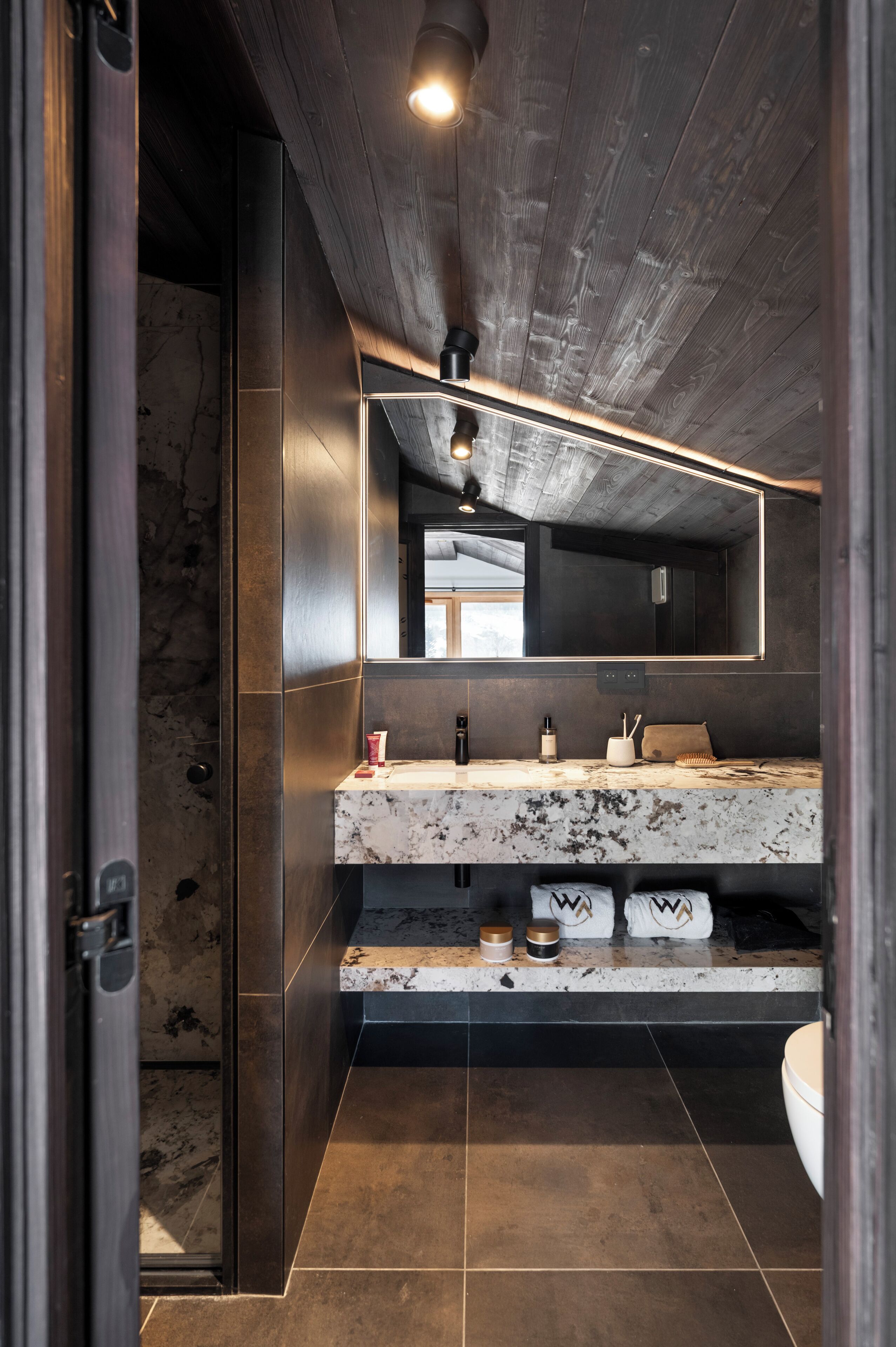 A modern bathroom with a marble countertop, a large mirror, and a wooden ceiling.