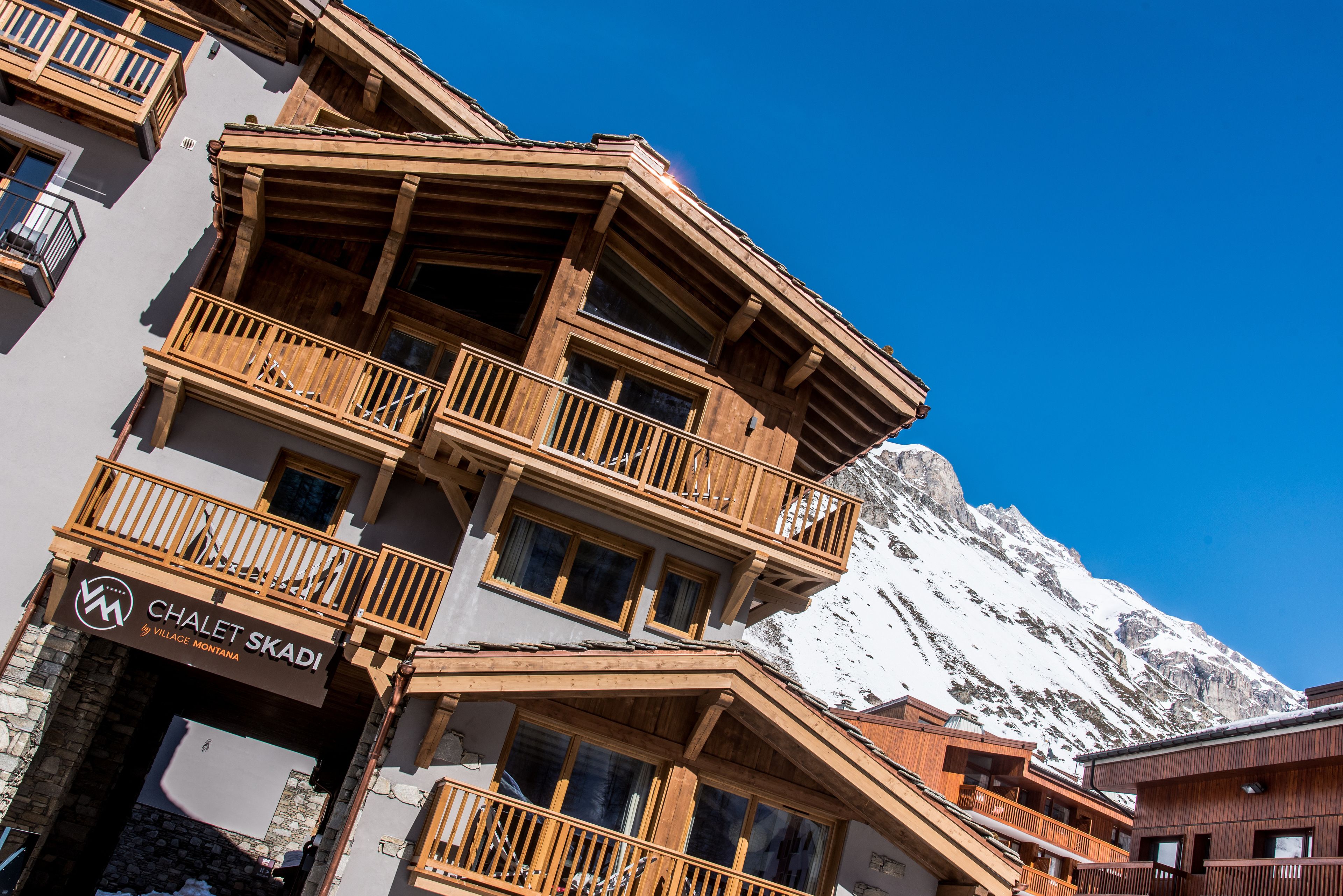 A multi-story wooden building with balconies and a sign reading "Chalet Skadi by Village Montana."