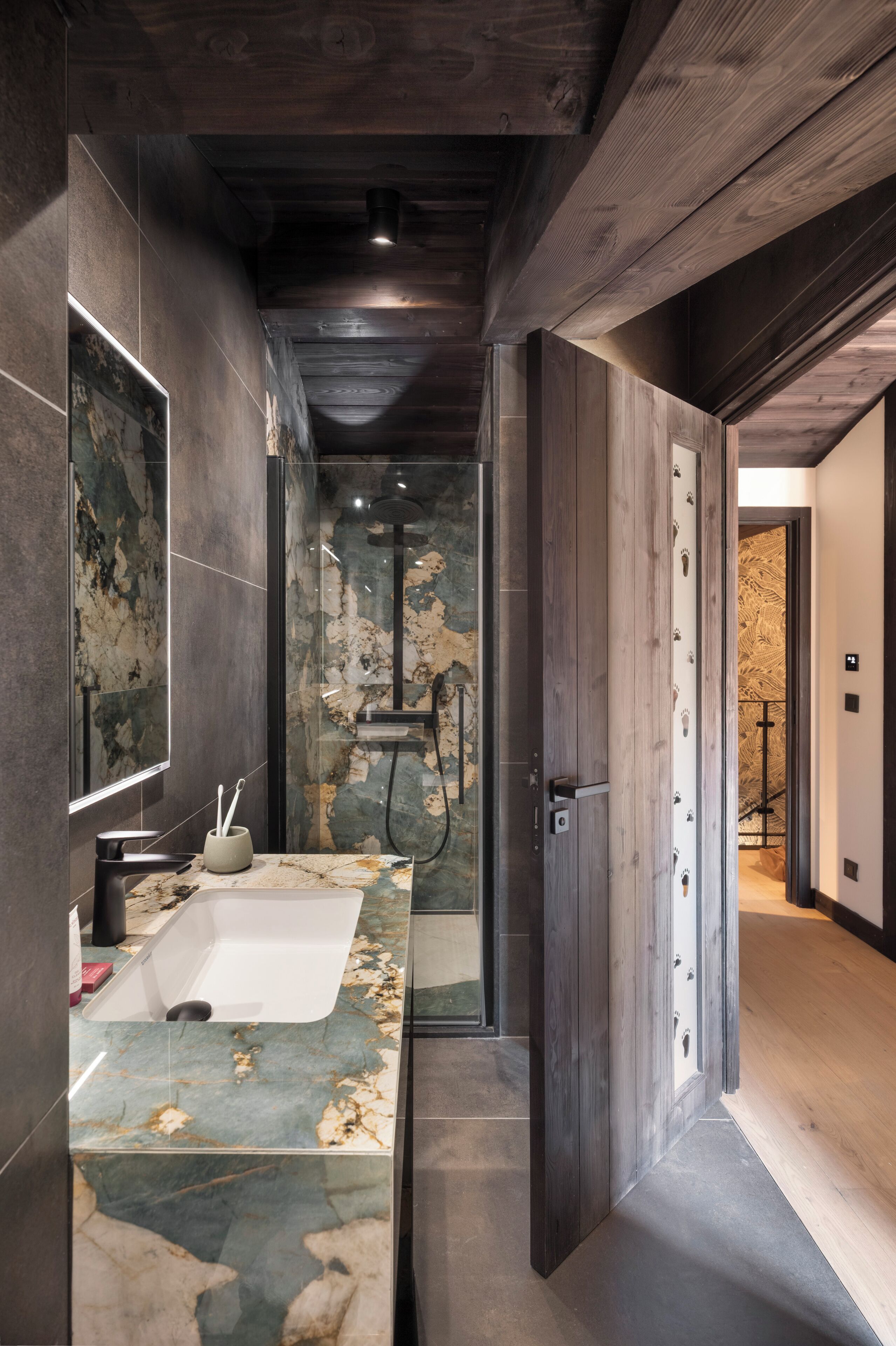 A modern bathroom with a marble sink, a shower, and a wooden door.