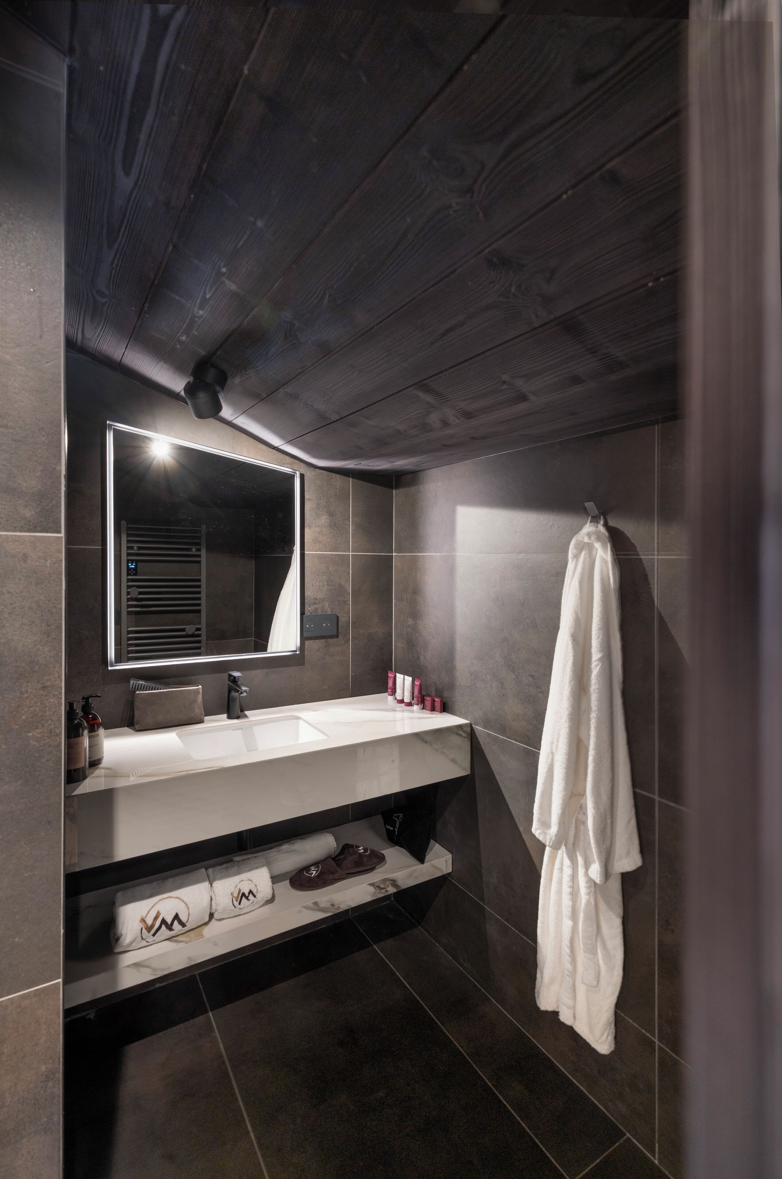 A modern bathroom with a large mirror, a white sink, a towel rack, and a shelf with shoes and toiletries.