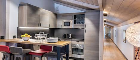 A modern kitchen with wooden cabinets, a stainless steel refrigerator, and a wooden dining table with bar stools.