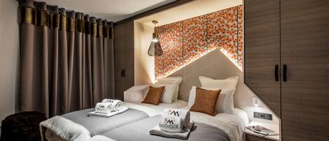 A modern hotel room with two beds, a large wardrobe, and a decorative wall.