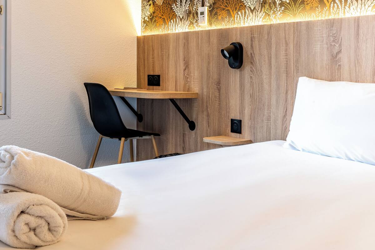 Habitació d'hotel amb un llit, escriptori, cadira i finestra amb vista a arbres.