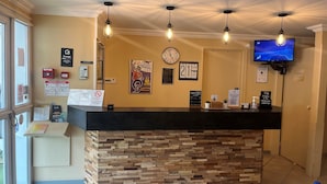 Zona de recepción de un hotel con un mostrador de madera, un reloj y un televisor en la pared.