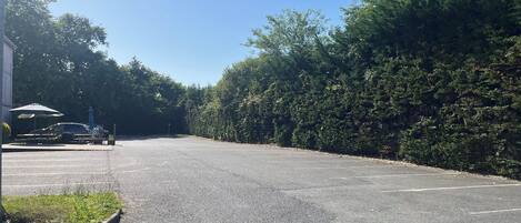 Een parkeerplaats met enkele auto's, omgeven door dichte bomen en een gebouw met een bord.