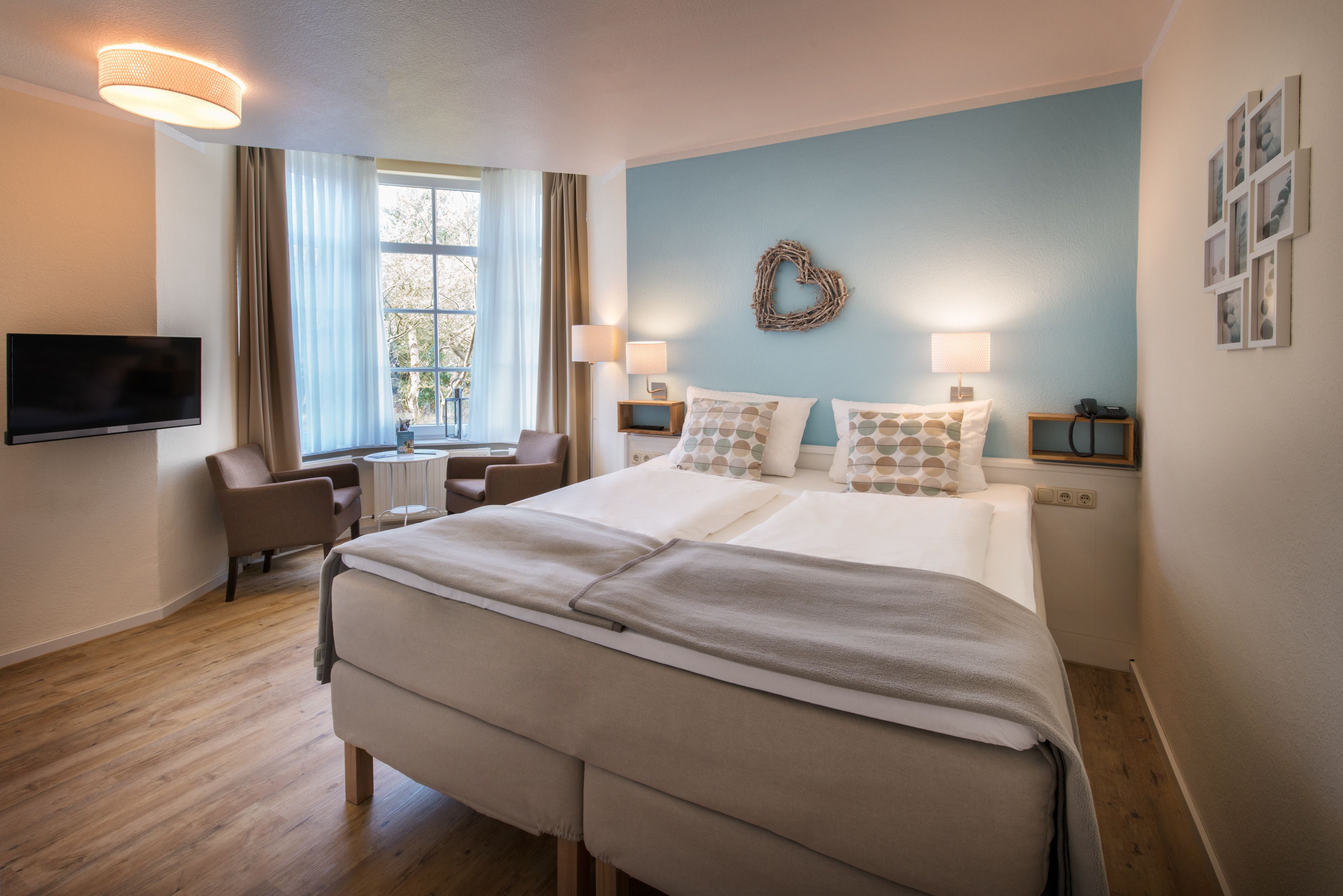 A hotel room with a large bed, two bedside tables, a TV, a desk, and a window with curtains.