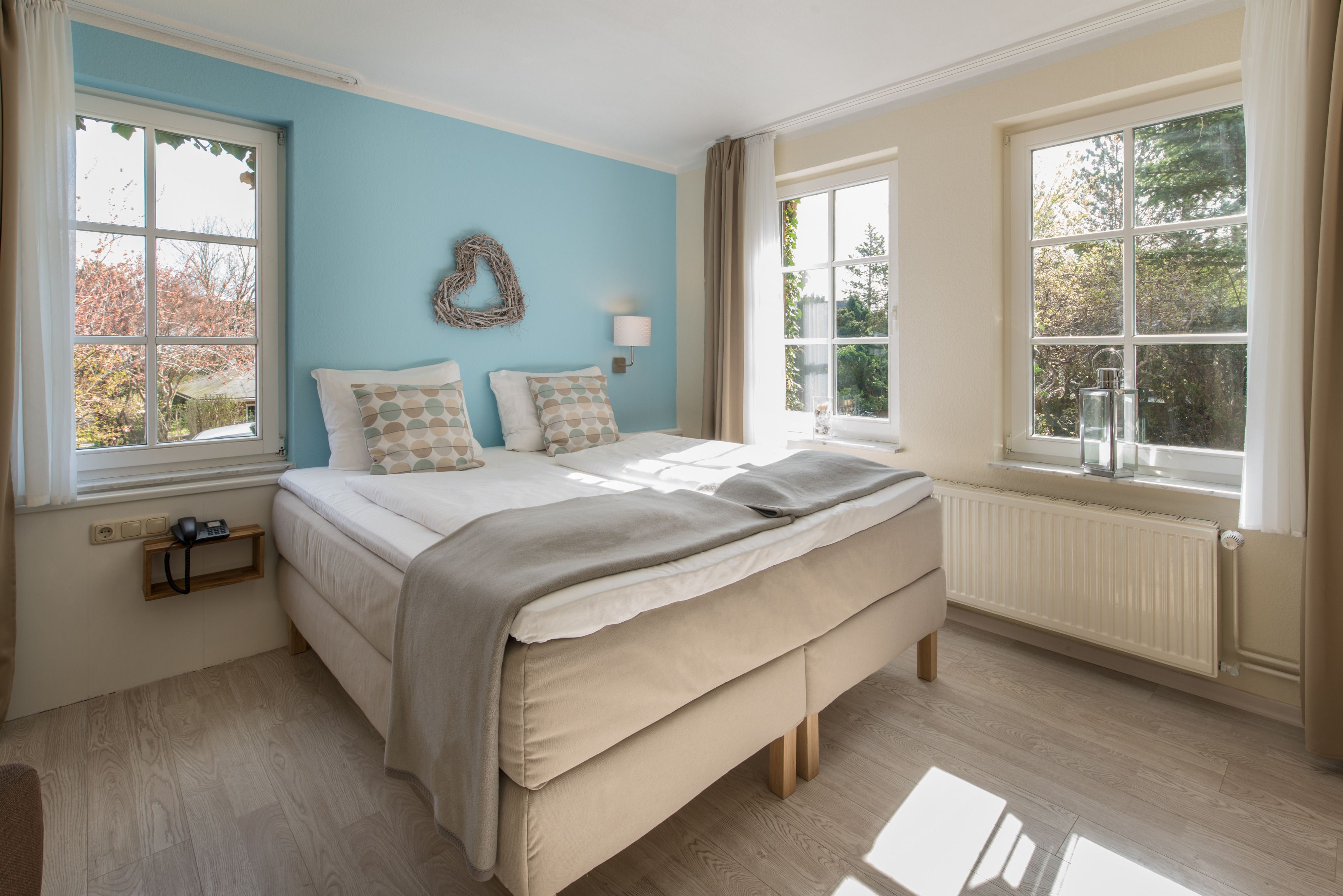A bedroom with a bed, two windows, a wall-mounted lamp, and a radiator.
