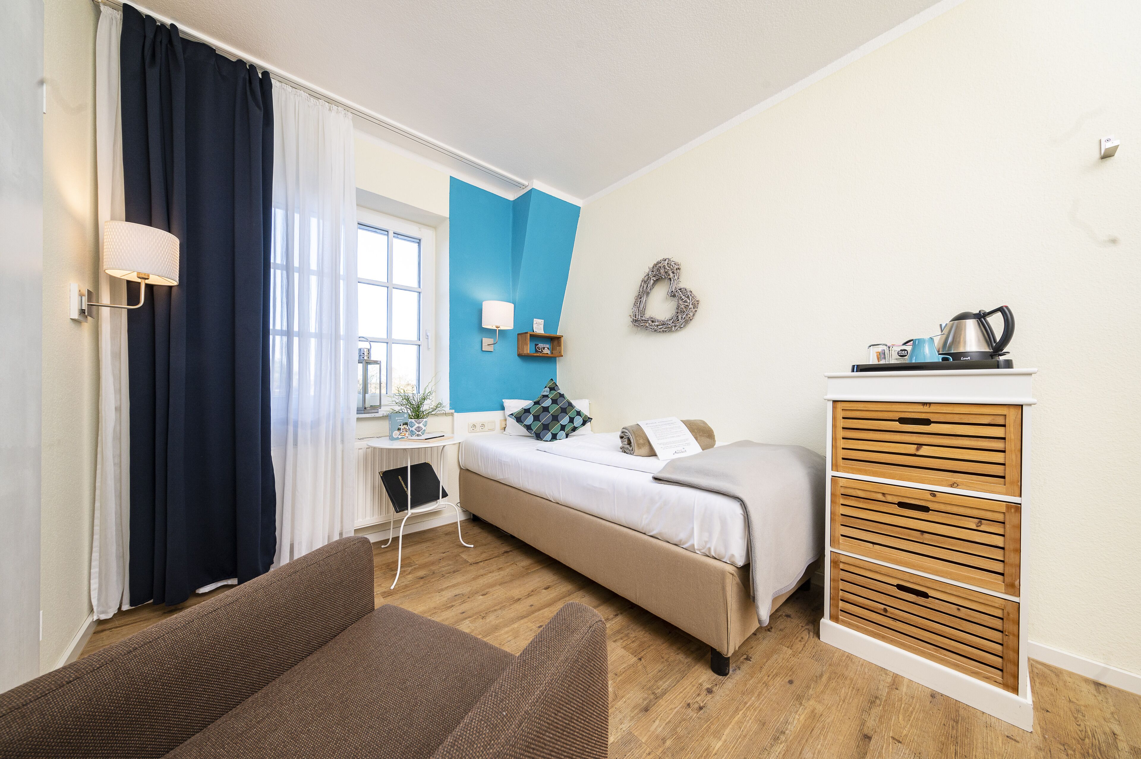 A bedroom with a bed, a desk, a chair, a dresser, and a window with curtains.