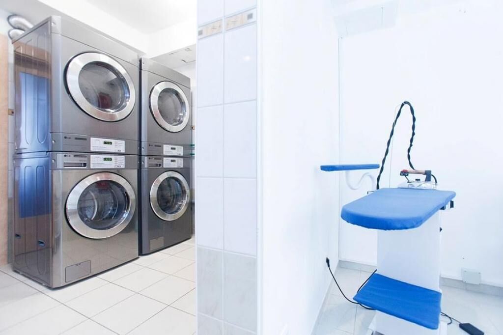 A laundry area with four stacked front-loading washing machines and a single ironing station.