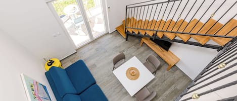 Un salon moderne avec un canapé bleu, une table blanche et un escalier à marches en bois.