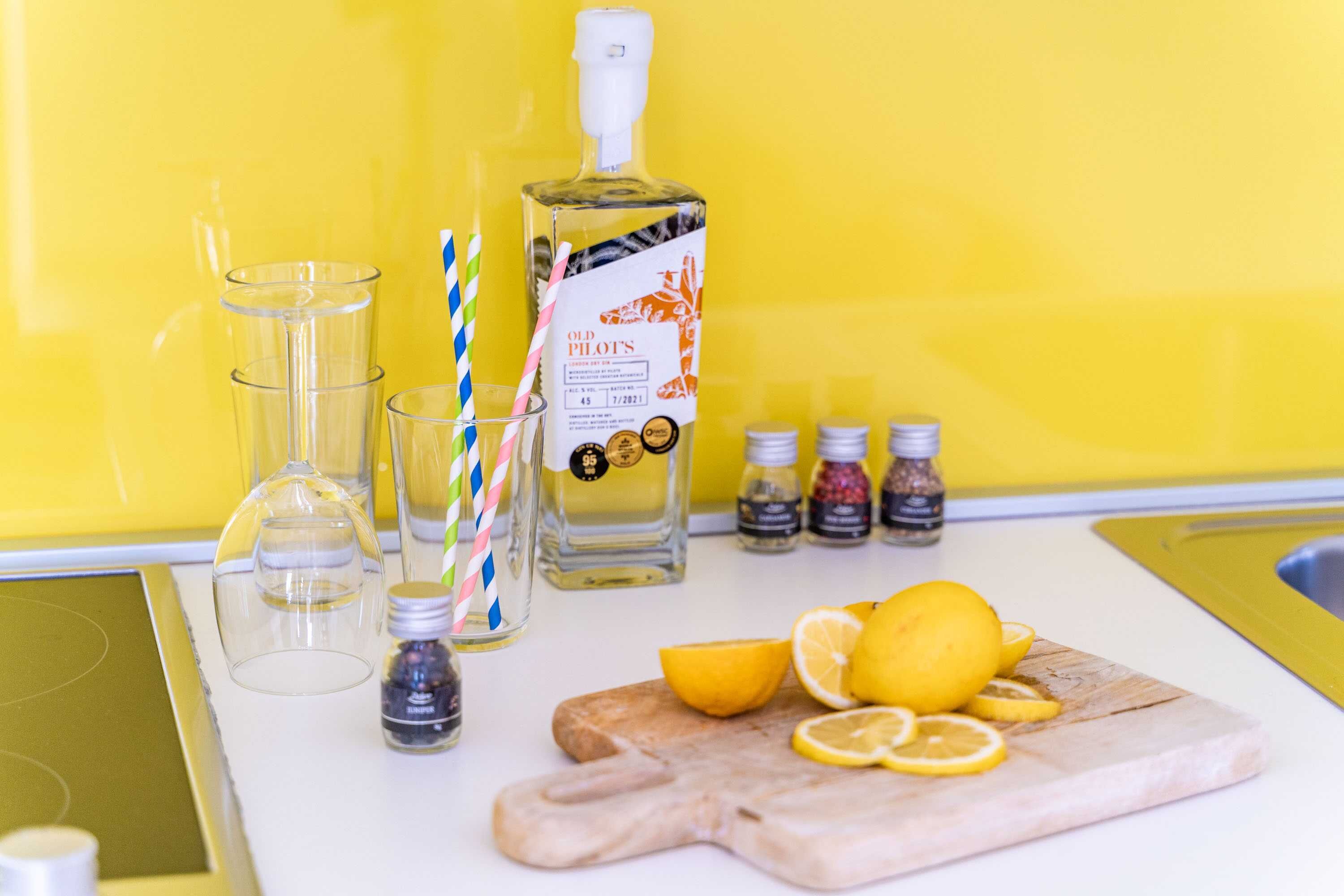 Una encimera de cocina con una botella de ginebra Old Pilot, vasos y rodajas de limón.