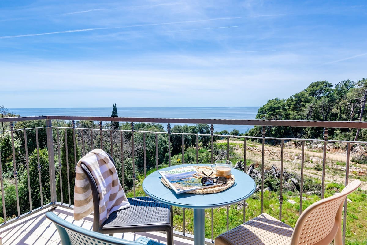 A balcony with a round table, chairs, and a view of the sea.