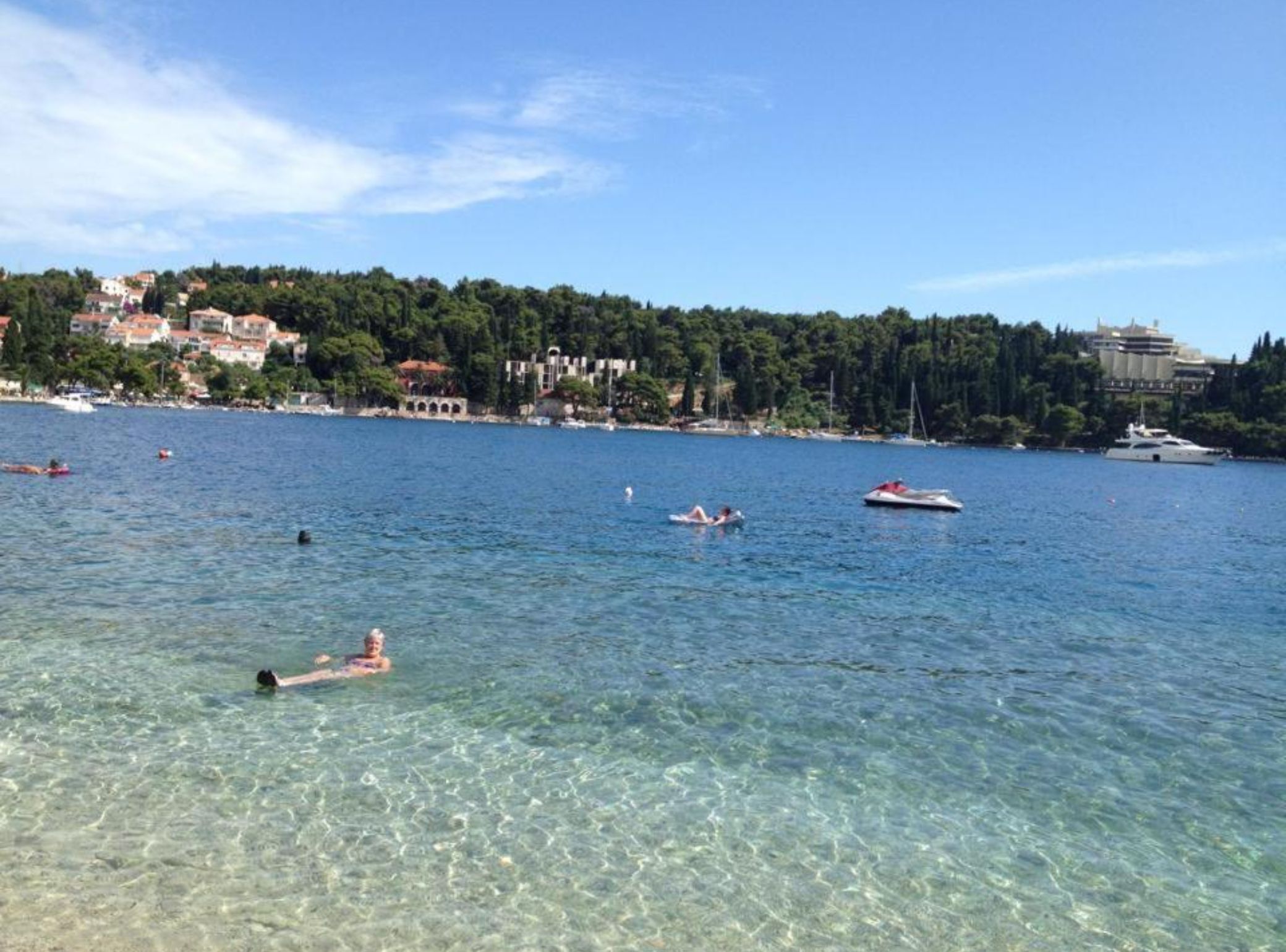 A clear waterfront with boats and people swimming.